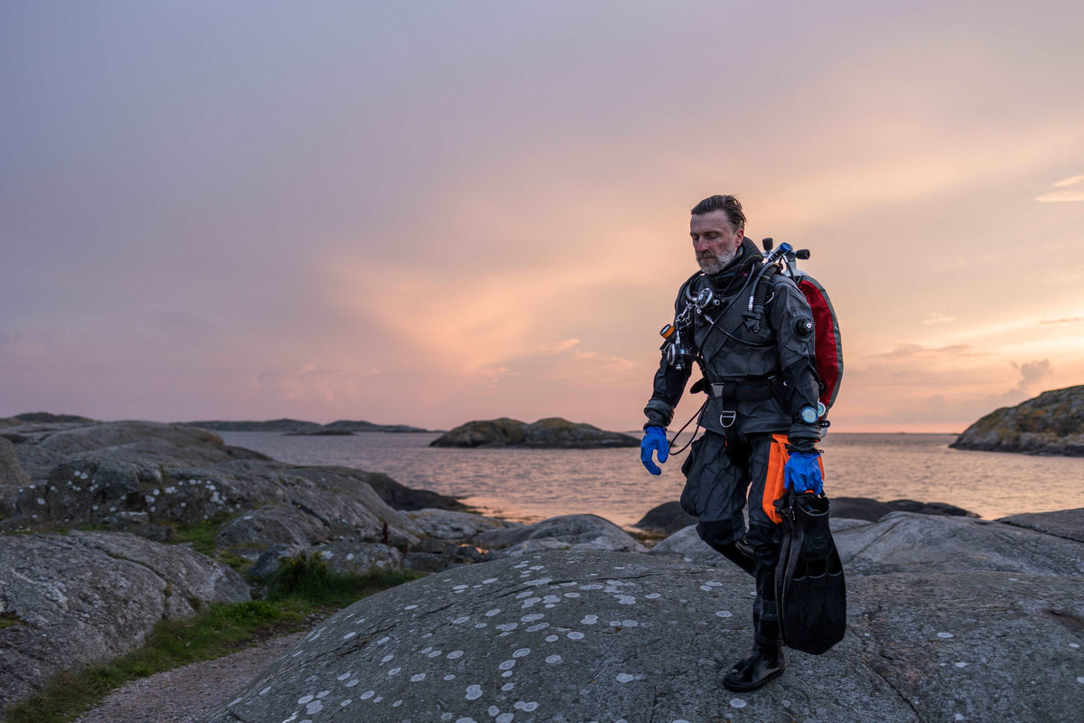 Diver walking along boulders in front of the ocean