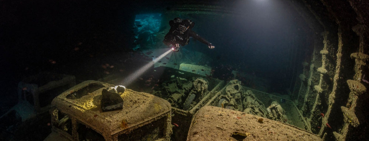 Diver inside of a shipwreck pointing a light at a boot
